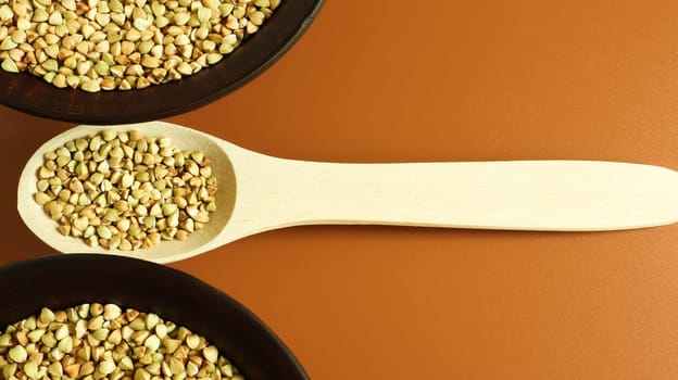 Raw green buckwheat in a brown clay plate and a wooden spoon. Vegan organic food concept. The concept of diet, weight loss, healthy and proper nutrition. Copy space for text. Top view, flat lay.