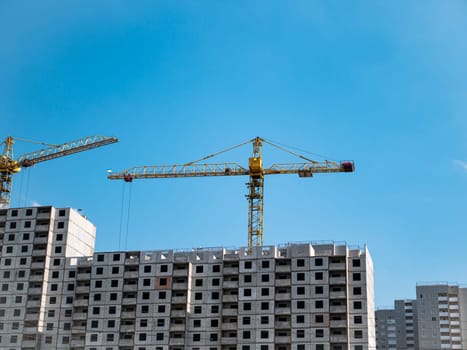 House construction with construction cranes on a background of blue sky. Construction and repair. Industry. Building sector. Poster. Advertising. Place for text. Template. Background image.