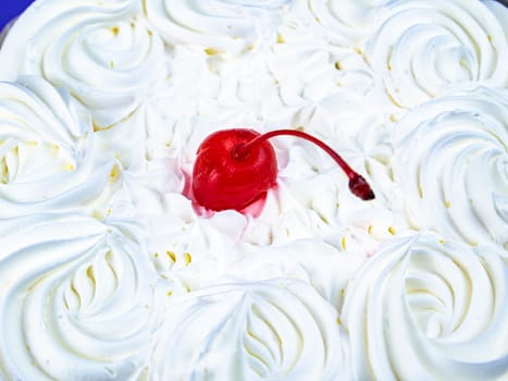 Red cherry from marmalade on white creamy flowers of a biscuit cake. Food photo. Dessert. Cake baking. Place for text. Shop window. Poster. Promotional event. Cake recipe.