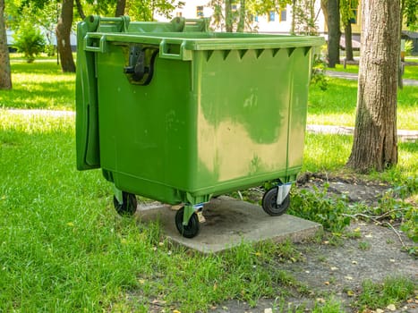 Green plastic trash can in a public park. Environment. City life. On open air. Natural conditions. Place for text. Background image. Ecology.