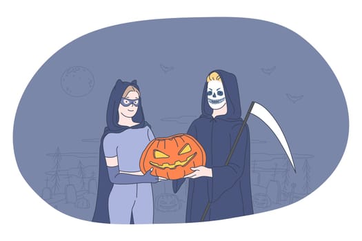 Celebrating Halloween holiday in spooky costumes concept. Young people cartoon characters in witch and death costume holding pumpkin in hands over cemetery at darl background