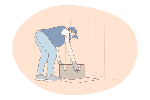 Contactless delivery, courier, online order concept. Young man courier deliveryman in protective medical mask and gloves putting parcel on floor near customer door. Parcel, logistics during pandemic