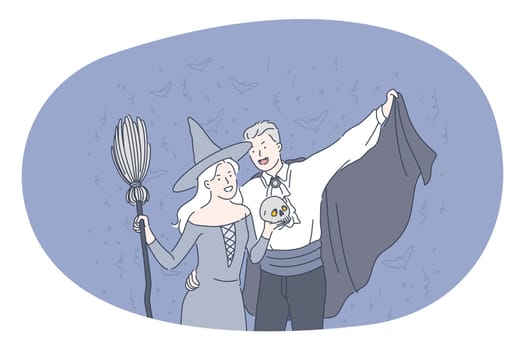 Celebrating Halloween holiday in spooky costumes concept. Young positive couple in festive costumes of witch and dracula standing holding skull in hands over flying bats at dark background