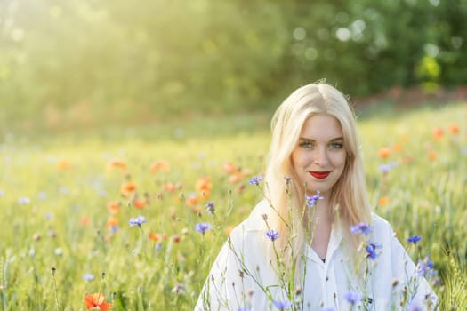 Blonde young woman posing in summer flower meadow.  Horizontally.