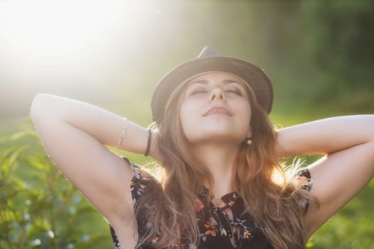 Attractive young girl wearing a hat enjoys with her hands behind her head. Horizontally.
