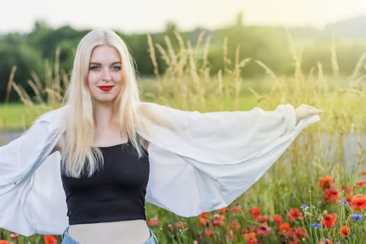 Smiling attractive young girl wearing a white shirt posing in a field with red poppies. Horizontally.