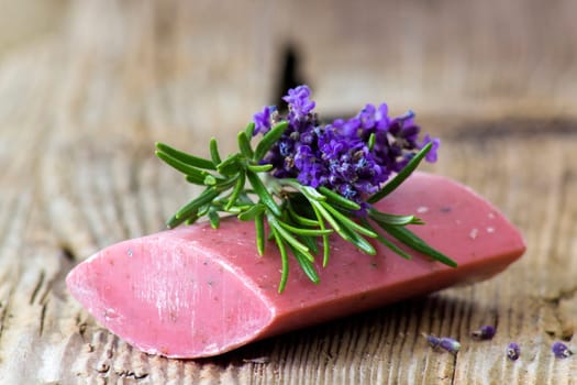 bar of natural soap, lavender flowers and rosemary on old wooden background