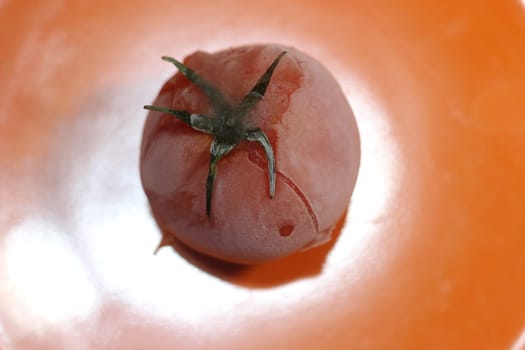 Tomato covered with hoarfrost on an orange background. Macro shot of a tomato on a white background.