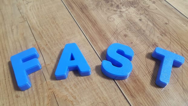 Plastic colored alphabets making words are placed on a wooden floor. These plastic letters can be used for teaching kids.