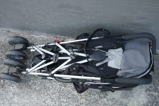 Black color baby stroller with head covering. Stroller is with concrete background