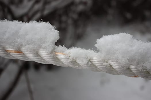 Snow flakes on rope in winter snowfall. Closeup macro view of snow on rope