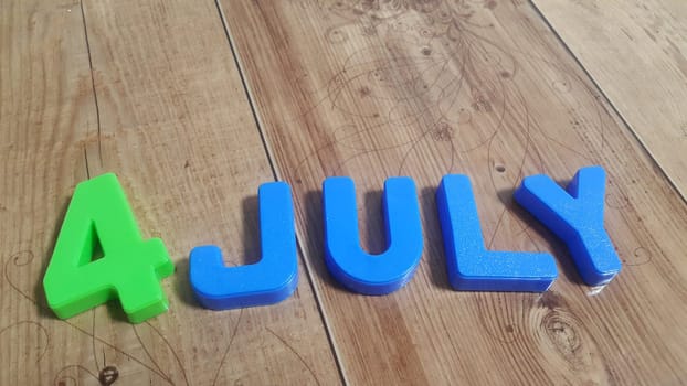Plastic colored alphabets making words 4 july are placed on a wooden floor. These plastic letters can be used for teaching kids.