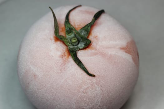 Tomato covered with hoarfrost on a white background. Macro shot of a tomato on a white background.