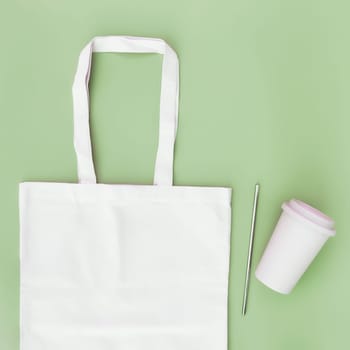 Eco white craft paper bag, metal drink straw, coffee cup on green background flat lay with copy space empty advertising area. Mock up for delivery service, reusable and recyclable resources concept