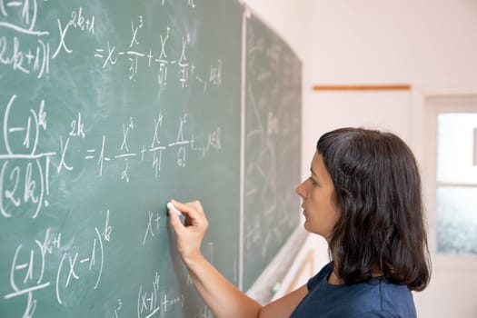 Teacher or student writing on blackboard during math lesson in school classroom.