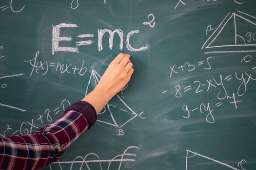 Close-up shot of a hand holding chalk and writing mathematical equations on the blackboard. Education concept.