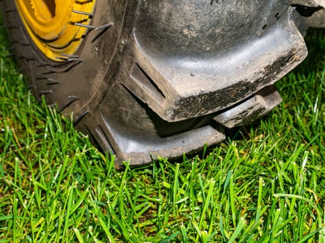 Agricultural tractor wheel on a green grass lawn. Car tire fitting. Vehicle tire rubber tread. Removing the green lawn of the city park with a tractor. Public park. Place for your text. Background.