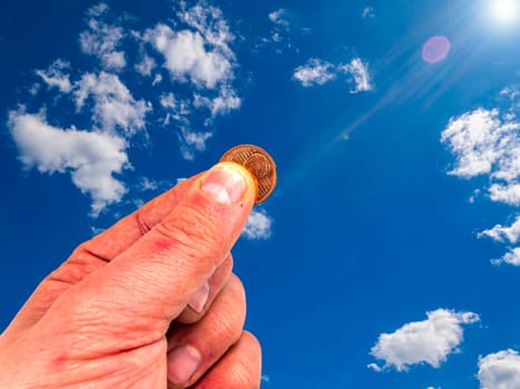 Hand with coins on a background of blue sky. God's gift. Prayer. Request for help. They ask for money. The hand of the giver. Sunbeams. Euro money. The image is in the background. Place for text.