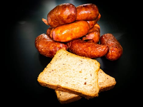 Smoked meat sausages with bread on a black background. Food photo. Recipe. Smoked meat. Fatty food. Home kitchen. Menu of dishes. Advertising photo of the store. Place for text. Poster.