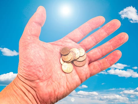 Hand with money coins on a background of blue sky. God's gift. Prayer. Request for help. Asking for money. Giver's hand. Sunbeams. Euro money. Background image. Place for text. Poster.