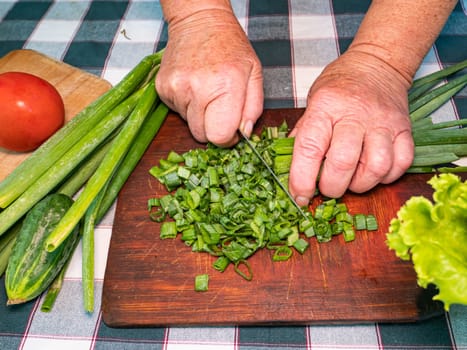 Slicing green onions with a knife on a cutting board. Green vegetable salad. Vegetables. Cook. Home kitchen. Vegetarian food. Recipe. Hands of a man. Vitamins