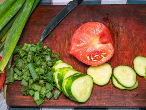 Slicing a red tomato with a knife on a cutting board. Green vegetable salad. Cook. Home kitchen. Vegetarian food. Recipe. Promotional photo. Hands of a man. Vitamins