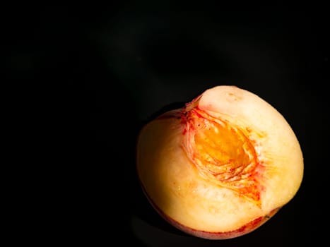 Half peach fruit on a black background. Peach bone. Food photo. Harvesting. Peach juice. Agriculture. Advertising photo of a shop window of a fruit shop. Place for your text. Background image.