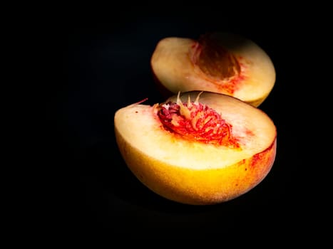 Half peach fruit on a black background. Peach bone. Food photo. Harvesting. Peach juice. Agriculture. Advertising photo of a shop window of a fruit shop. Place for your text. Background image.