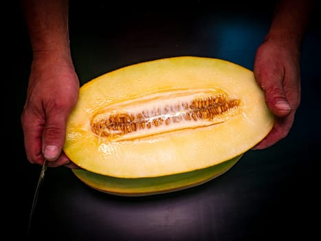 A yellow melon cut with a knife in the hands of a man. Food photo. Melon culture. Agriculture. Place for your text. Black background. Background image. Shchablon. Poster. Vegetarian food.