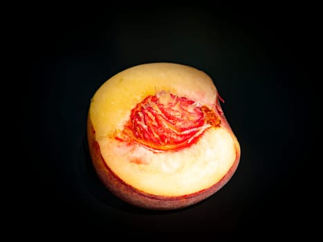 Half peach fruit on a black background. Peach bone. Food photo. Harvesting. Peach juice. Agriculture. Advertising photo of a shop window of a fruit shop. Place for your text. Background image.