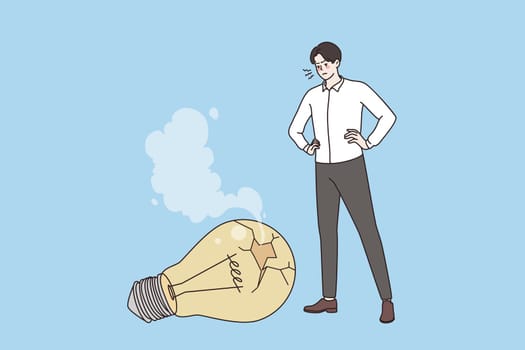 No idea, challenge and crisis concept. Young frustrated Businessman standing looking at fallen broken light bulb feeling problems in creativity vector illustration