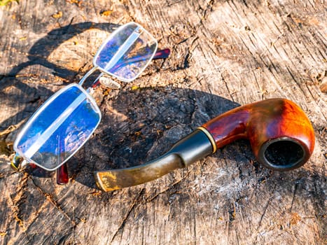 Smoking pipe for tobacco and glasses on a wooden table. Wooden pipe for smoking tobacco. Smoker's tool. Bad habits. Nicotine addiction. Nicotine in cigarettes. Place for your text. Background.