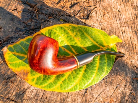 Wooden smoking pipe for tobacco and autumn leaf. Pipe for smoking tobacco. Smoker's tool. Wooden table. Bad habits. Nicotine addiction. Nicotine in cigarettes. Background image. Poster.