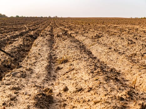 A plowed agricultural field against the cloudy skyline. Plowed potion in a farm field. Autumn season. Trees on the horizon. Cloudy sky. Preparation for sowing agricultural crops. Background image.