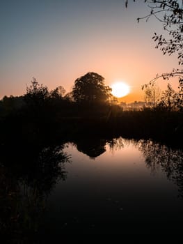 The water surface of the river and the sunrise. Dawn of the morning sunrise. Orange sunny sunset. Evening dawn. The water surface of the river. River reeds. Fishing. Horizon. Fog. Fishing place.