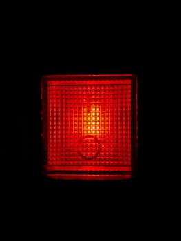 Glowing red plastic lamp in the dark. Signal light red. Night illumination. Black background. Electrical appliance button. Emergency lighting. Electric light. Background image.