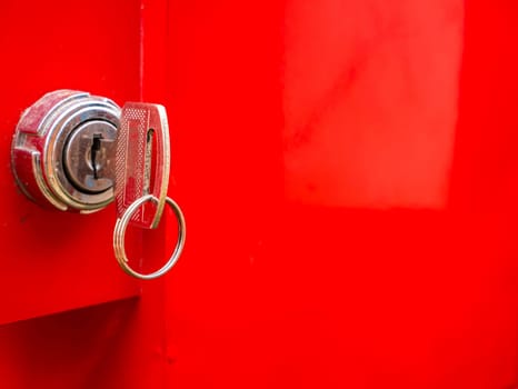 Key in the keyhole on a red background. Car ignition key. Door lock. Open or close the door. Property protection. Safety system. Private property. Bank safe. Metal safe. Luggage storage.