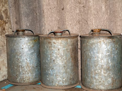 Old stainless steel canisters for storing fuels and lubricants. Metal cans for gasoline. Tank for technical oil. Diesel fuel. Car garage. Refilling the car. Place for text. Background image.