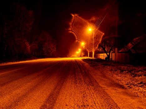 Night winter snowy road for cars in the light of lanterns. Snow on a country road. Street lights. Winter period. Night time. Night street lighting. Lens flare. New Year. Christmas holidays. Snowstorm.