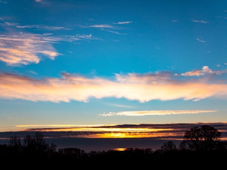 Morning sunrise on the horizon with clouds. Morning dawn. Evening sunset. Evening time of the day. Cloudy horizon. Shadows of trees. Natural landscape. Blue sky with clouds. Day and night. Scenery.
