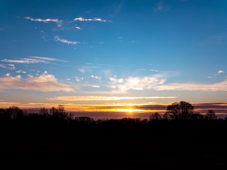 Morning sunrise on the horizon with clouds. Morning dawn. Evening sunset. Evening time of the day. Cloudy horizon. Shadows of trees. Natural landscape. Blue sky with clouds. Day and night. Scenery.