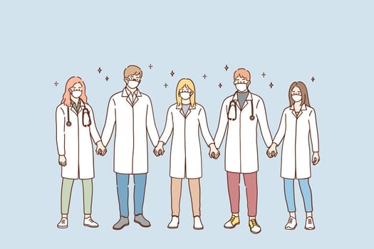 Doctors teamwork, uniting efforts against COVID-19 pandemic concept. Group of young doctors in protective medical face masks standing and holding hands in team during pandemic vector illustration