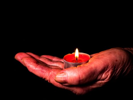 Flame of fire of burning wax candles in the palms of the hands. Wax candles. Flame of burning fire. Day of Remembrance. A minute of silence. Memorial Day. Black background. Human hands.