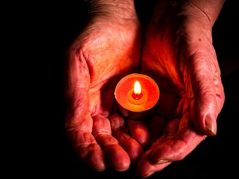 Flame of fire of burning wax candles in the palms of the hands. Wax candles. Flame of burning fire. Day of Remembrance. A minute of silence. Memorial Day. Black background. Human hands.