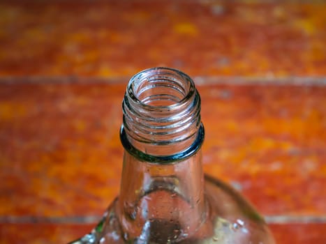 Glass bottle for vodka with a handle on a wooden background. Neck of a glass bottle. Alcohol. Glassware for alcohol. Bad habits. Alcoholism. Background image. Container with a handle.
