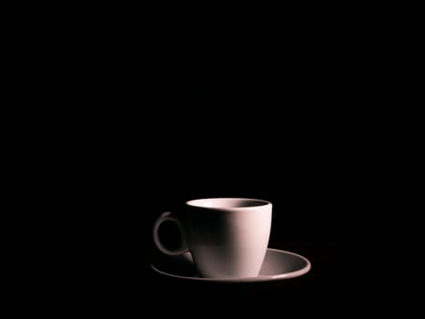 White ceramic coffee cup with saucer on a black background. Coffee cup and saucer. White ceramic dishes. Hot drinks. Kitchenware. Preparing a hot drink. Hot tea. Background image. Poster. Showcase.