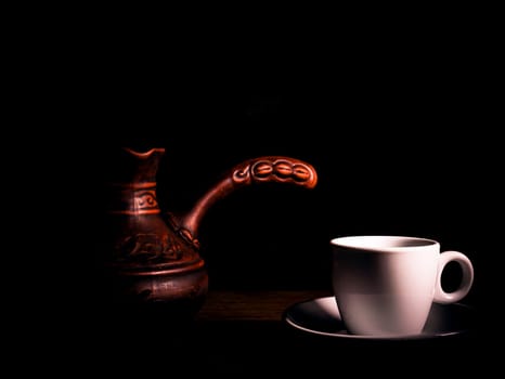 White ceramic coffee cup with saucer and coffee maker on a black background. Coffee cup and saucer. White ceramic dishes. Hot drinks. Kitchenware. Preparing a hot drink. Hot tea. Background image.