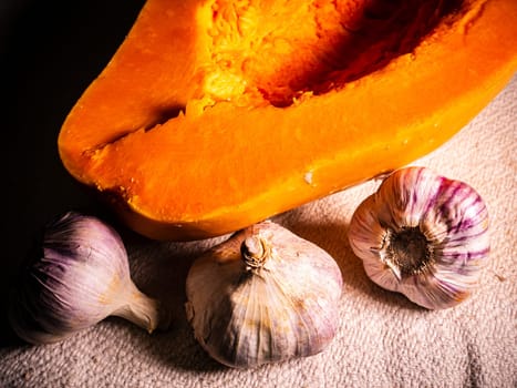 Orange pumpkin and garlic vegetable on a black background. Harvest vegetables. Head of garlic. Halloween orange pumpkin. Halloween holiday. Agriculture. Background image. Food photo.