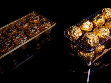 A box of round chocolates in a golden wrapper on a black background. Round candies. Golden color. A holiday gift. Birthday. Food photo. Sweet food. Happy birthday. Background image. Chocolate.