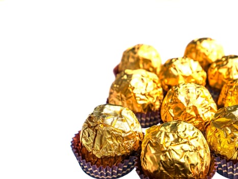 Round chocolate candies in a golden foil wrapper on a white background. Sweet cake. Golden wrapper. Shiny foil. Candy wrapper. Sweet dessert. White background. Background image.